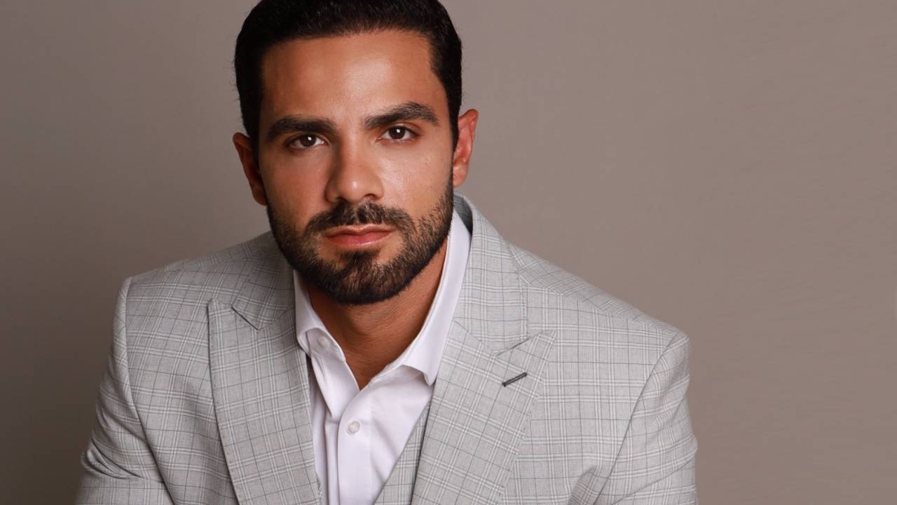 Homem de barba com terno cinza claro posa sentado