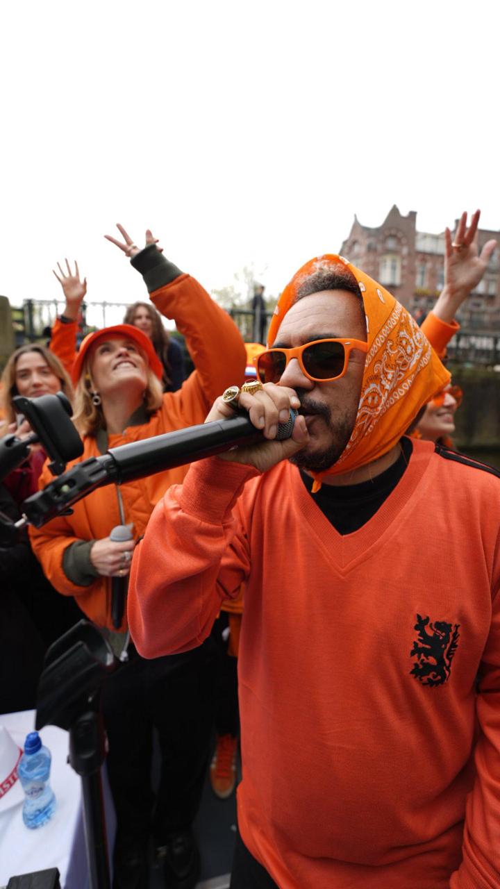 King’s Day em Amsterdã com Marcelo D2 Crédito Raphael Felisbino-Divulgação (6) Foto de barco com pessoas em tom laranja no canal de Amsterdã com foco em cantor segurando microfone