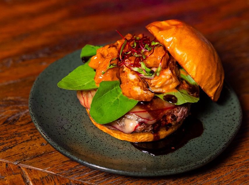Hamb&uacute;rguer em prato escuro e mesa de madeira