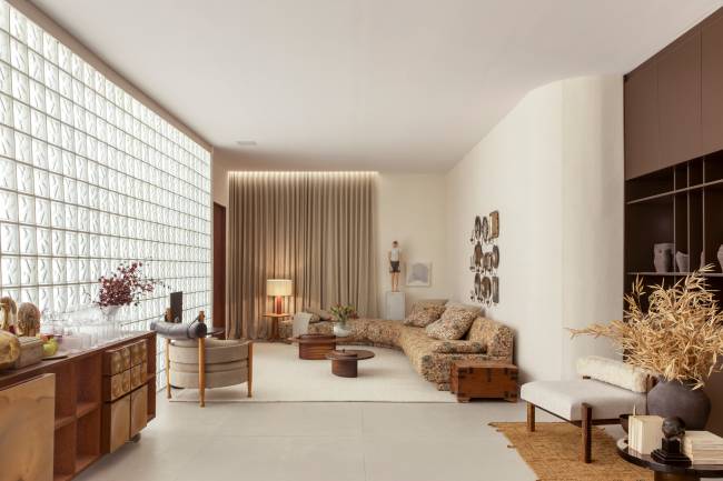 Design sob holofote: poltrona Vivi destacada por parede de tijolo de vidro em ambiente de Léo Shehtman