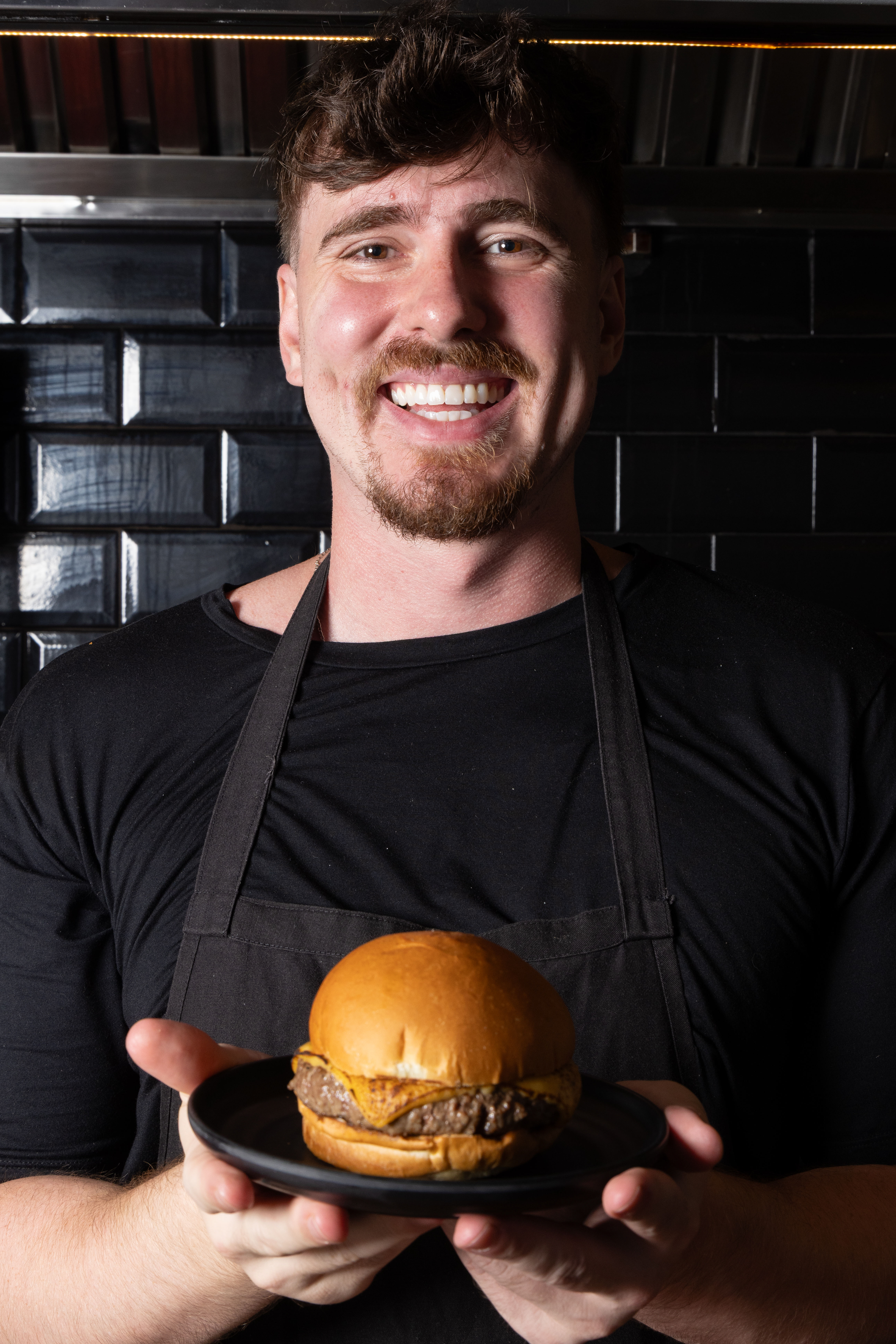 homem sorrindo com hamb&uacute;rguer na m&atilde;o