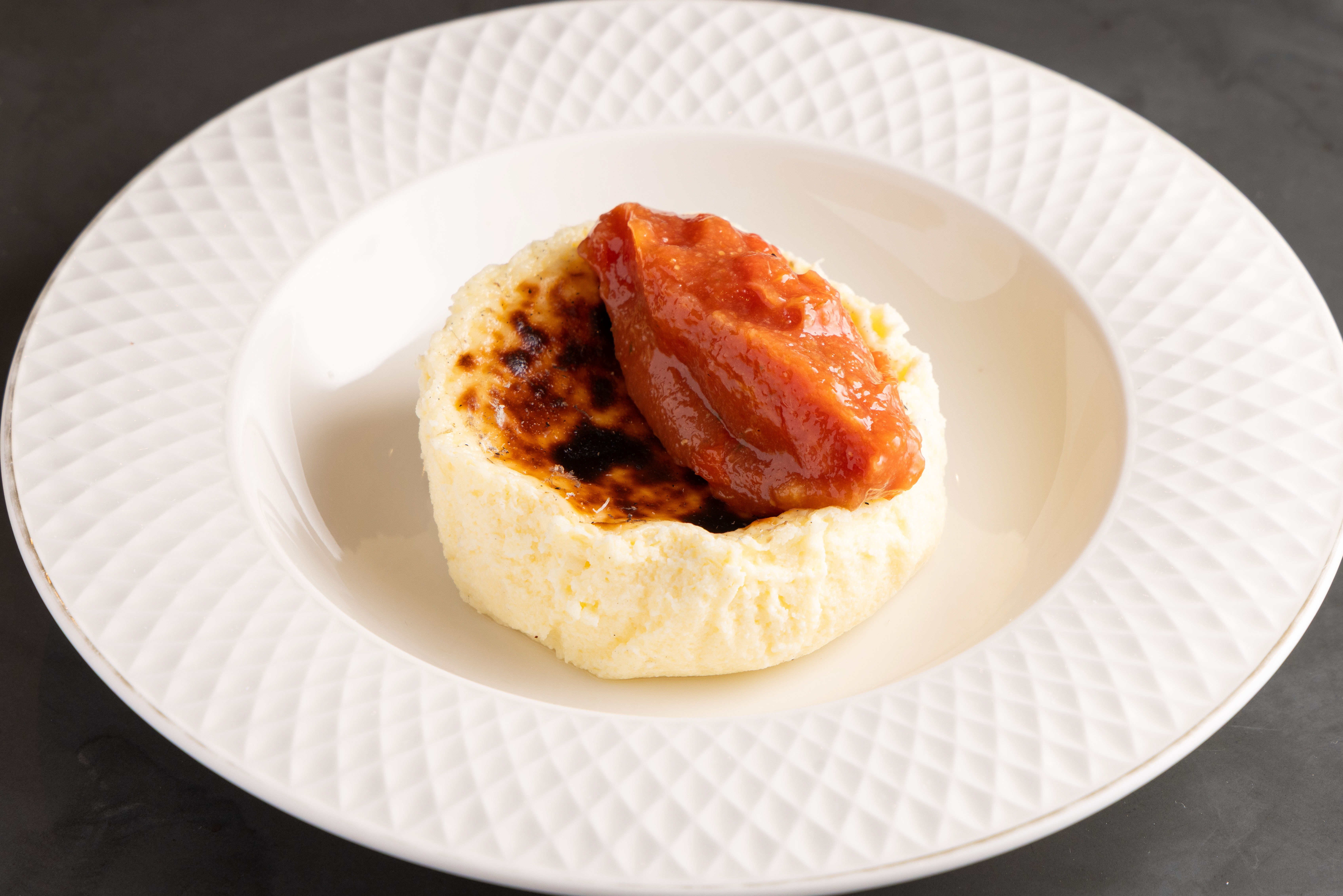 Doce de queijo cremoso, com topo caramelizado e uma colher de goiabada cremosa, servido em prato branco com borda texturizada