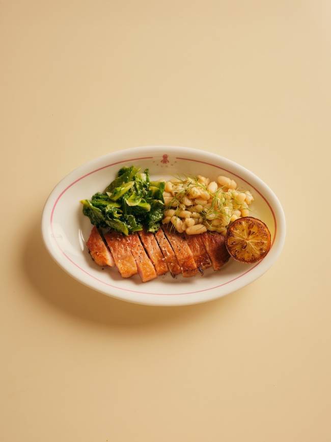 Prato oval branco com borda rosa, contendo carne grelhada fatiada, feij&atilde;o branco com endro, couve refogada e uma rodela de lim&atilde;o grelhado